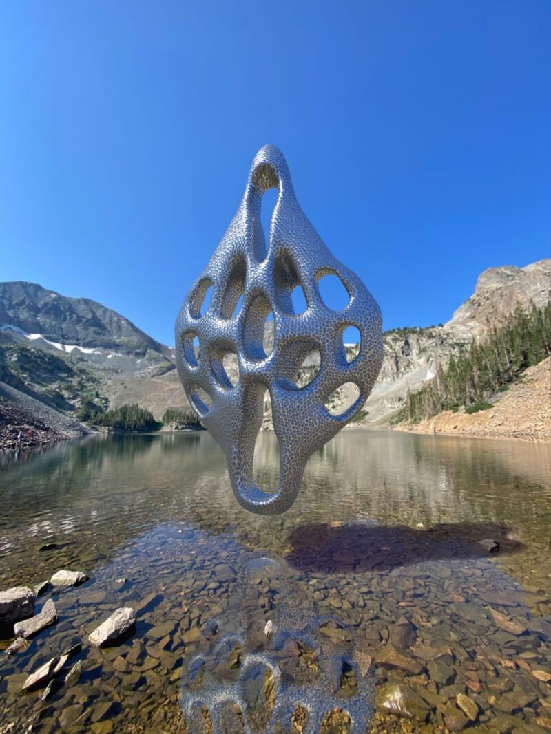 Apstraktna VR 3D skulptura postavljena u realnoj fotografiji planinskog pejzaža iznad mirnog jezera