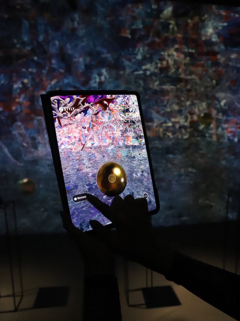 Osoba koristi tablet da prikaže AR svet Nadine Kolodziey sa zlatnom sferom i raznobojnim apstraktnim elementima