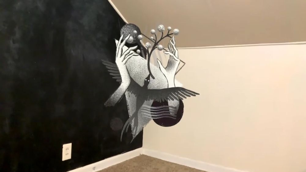 Digitalna crno-bela AR figura sa rukama, krilima i granom pojavljuje se u sredini jednostavne sobe